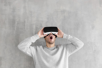 Amazed young man playing video games in VR goggles or 3d glasses, wearing virtual reality headset for on his head