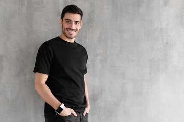 Horizontal portrait of young man standing isolated against gray textured wall feeling confident and looking optimistic in casual clothes, copyspace for advertising your goods or services