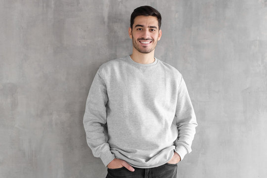 Young man in oversized sweatshirt isolated on textured gray wall background