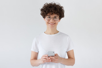 Portrait of beautiful young woman holding smart phone, looking at camera, isolated on gray background