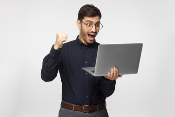 Excited business man looking at laptop screen with mouth wide open, celebrating his win, isolated...