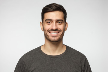 Close-up portrait of smiling handsome young man in casual t-shirt, isolated on gray background