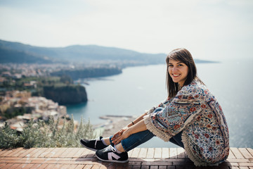 Happy woman traveler smiling at italian coast view.Woman traveling to European south coast.Enoying sunny weather medditerranean seaside