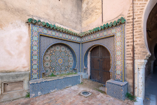 Traditional ornamental drinking fountain in medina in Meknes, Morocco. Decorated fountain with mosaic tiles. Ornate mosaic and traditional Islamic religious art. Ancient oriental Moroccan