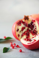 Ripe pomegranate fruit with green leaves on grey concrete background. Banner with copy space. Vegan, healthy diet concept