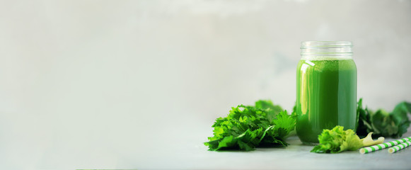 Bottle of green celery smoothie on grey concrete background. Banner with copy space. Square crop....