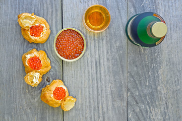 Eclairs with red caviar, caviar in a tin, a bottle and a glass of cognac on a wooden rustic vintage background.
