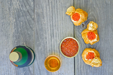 Eclairs with red caviar, caviar in a tin, a bottle and a glass of cognac on a wooden rustic vintage background.