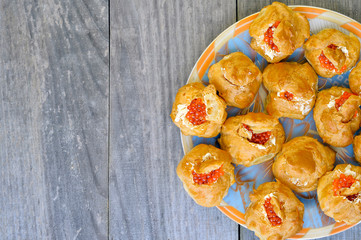 Eclairs with red caviar are laid out on a colored plate on a wooden rustic vintage background. Background, copy space