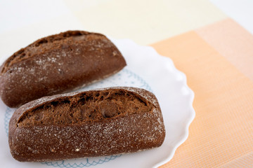 Air black buns with coriander on a white plate, on a background of lemons and tomatoes
