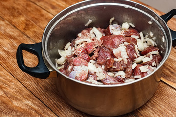 Marinated meat with onion in pan on wooden background. Preparation of raw meat for barbecue. The view from the top.