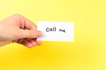 Call me text on a card in woman hand  on a yellow background.