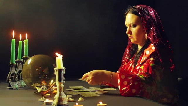 A young gypsy in a fortune-telling saloon by candlelight lays out cards for divination on the table