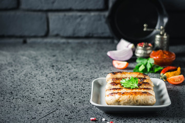Grilled sausages in cast iron skillet with herbs, sauce and spices on dark background. Selective focus, space for text.
