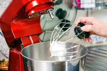 A woman is cooking in her kitchen, about to bake a cake. In a red food processor whipped chicken proteins with sugar
