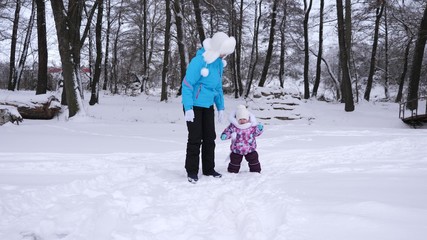 Fototapeta na wymiar Mom leads hand of her little daughter during walk through snow covered park in winter. Mother walks with child who is naughty and crying. Christmas.
