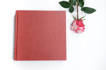 Red leather covered wedding album or wedding book and one beautiful rose lies on white background