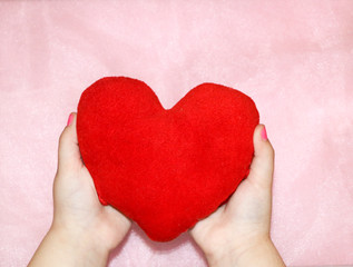 soft red heart in the hands of a child on a pink background