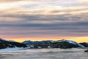 Mountain hut with forzen lake at sunset
