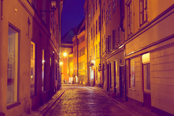 Fototapeta na wymiar The narrow cobblestone street with medieval houses of Gamla Stan historic old center of Stockholm in the evening twilight sunset. Toned image