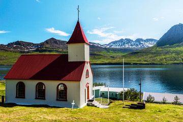 The church of Mjoifjordur village and the landscape of the fjord and mountain cost at the background