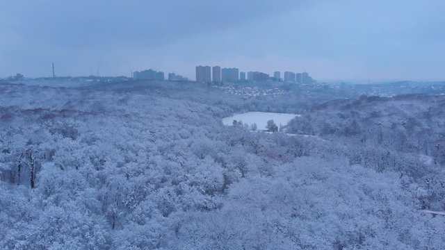Beautiful city park covered with snow with appartment buildings in the background, aerial footage.