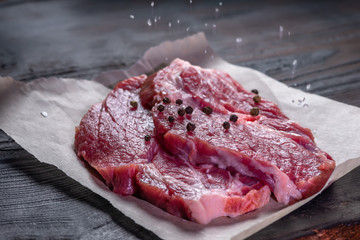 portion of fresh boneless raw pork meat strewing salt and peppers on wooden table, close up
