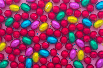 Fototapeta na wymiar Easter eggs in colorful foil chocolate Easter eggs and sprinkles over pink, holiday background