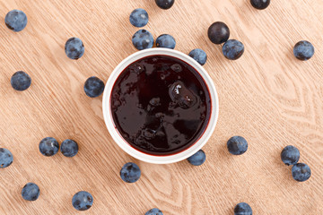 The composition of sweet organic sloe jam in a bowl with a wooden background. Top view - obrazy, fototapety, plakaty