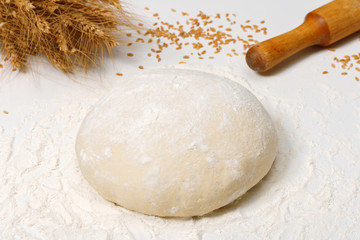 Raw fresh dough in the flour and ears of wheat on a white background