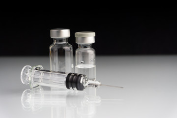 Medical syringe and vial on dark background with selective focus and crop fragment