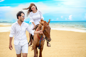 Young couple in love walking with the horse at sea beach on blue sky . honeymoon tropical sea...