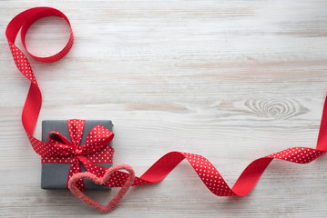 Grey gift box with red ribbon on a white wood backgraund