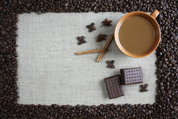 Filiżanka kawy otoczona ziarnami kawy, obok cynamon i czekoladowe ciastka