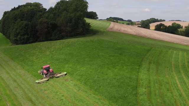 Aerial view of a tractor mowing a green fresh grass field on a sunny day.