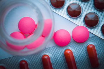 Blisters with colorful tablets and pink pills are poured from a glass jar on a white blue background. The view from the top.