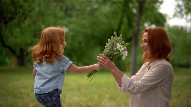 Beautiful kid gives flowers to smiling mother