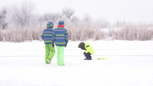 Happy children in colorful clothes run plane glider on frozen snow-covered river. Boys are competing with each other. Winter holidays in  village.