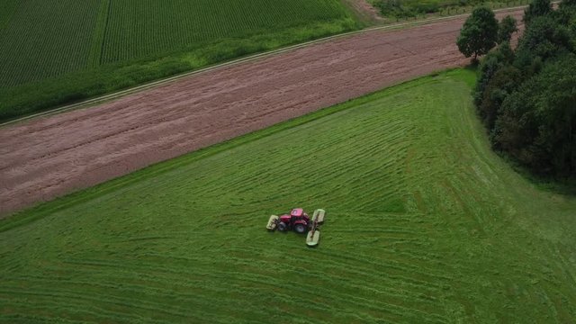 Aerial view of a tractor mowing a green fresh grass field on a sunny day.