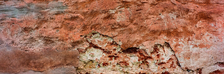 brick wall covered with old crumbling cement plaster with traces of paint.