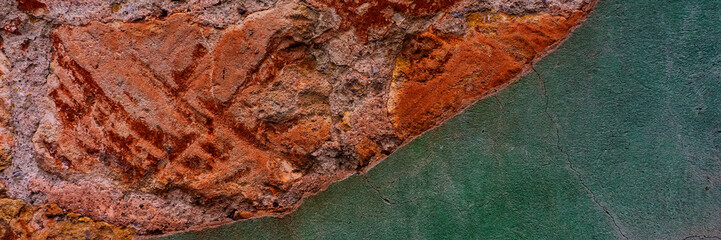 brick wall covered with old crumbling cement plaster with traces of paint.