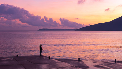 Fototapeta premium Man Fishing Alone on Pier At Sunset