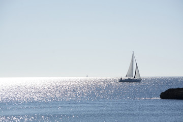 Backlit sailboat on bright and sunny sea with horizon