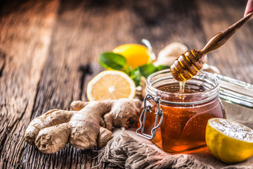 Honey jar dipper ginger lemon and mint herbs on wooden table