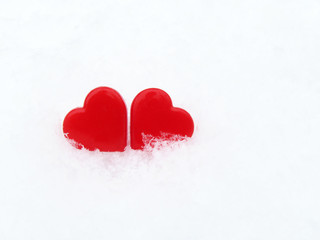 Fototapeta premium Two Valentine hearts in the snow, red symbols of love. Background for Valentines day greeting card, concept of romantic celebration