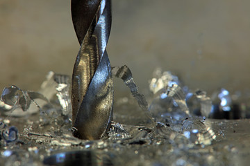 close up of an industrial drill bit drilling in to alluminium withj metal swarf
