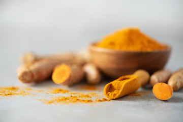 Turmeric powder in wooden bowl and fresh turmeric root on grey concrete background. Banner with copy space