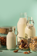 Glass bottles of vegan plant milk and almonds, nuts, coconut, hemp seed milk on blue background. Banner with copy space. Dairy free milk substitute drinks and ingredients