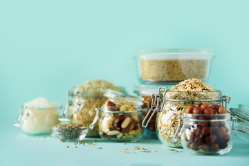 Vegan health food over blue background with copy space. Nuts, seeds, cereals, grains in glass jars....