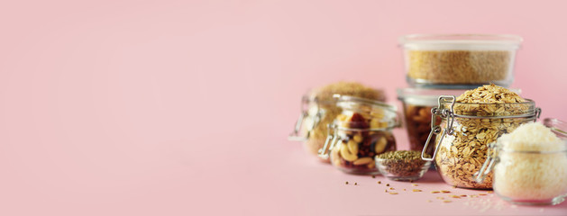 Vegan health food over pink background with copy space. Nuts, seeds, cereals, grains in glass jars....